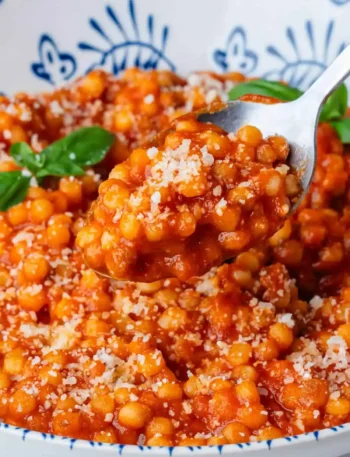 Fregola Sarda mit Tomatensoße, Parmesan und Basilikum auf einem Löffel serviert