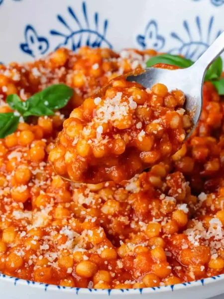 Fregola Sarda mit Tomatensoße, Parmesan und Basilikum auf einem Löffel serviert