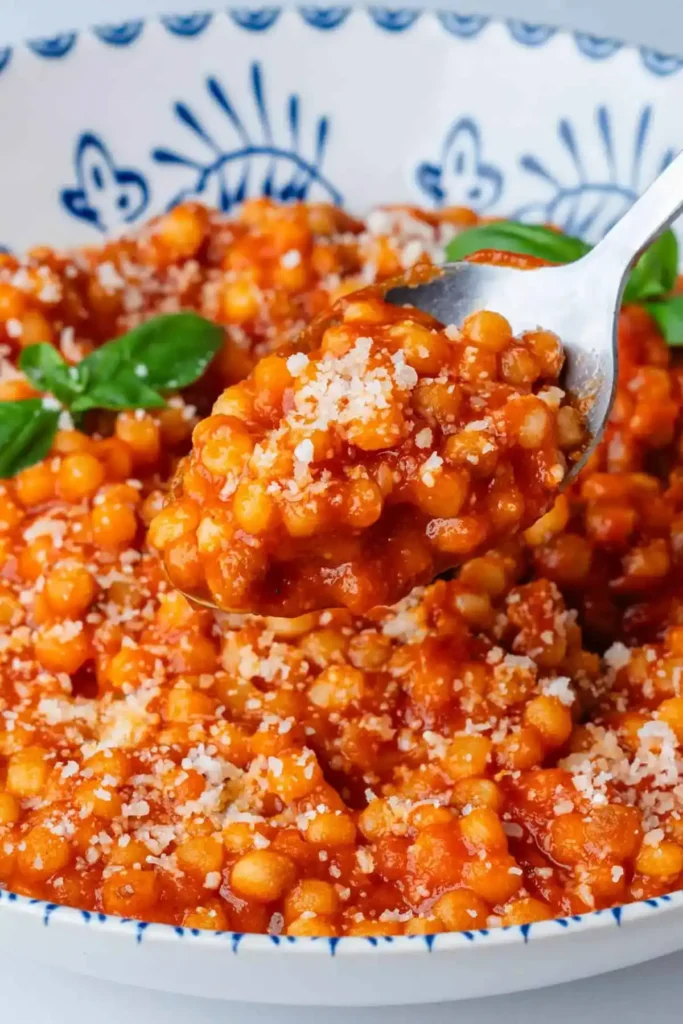 Fregola Sarda mit Tomatensoße, Parmesan und Basilikum auf einem Löffel serviert