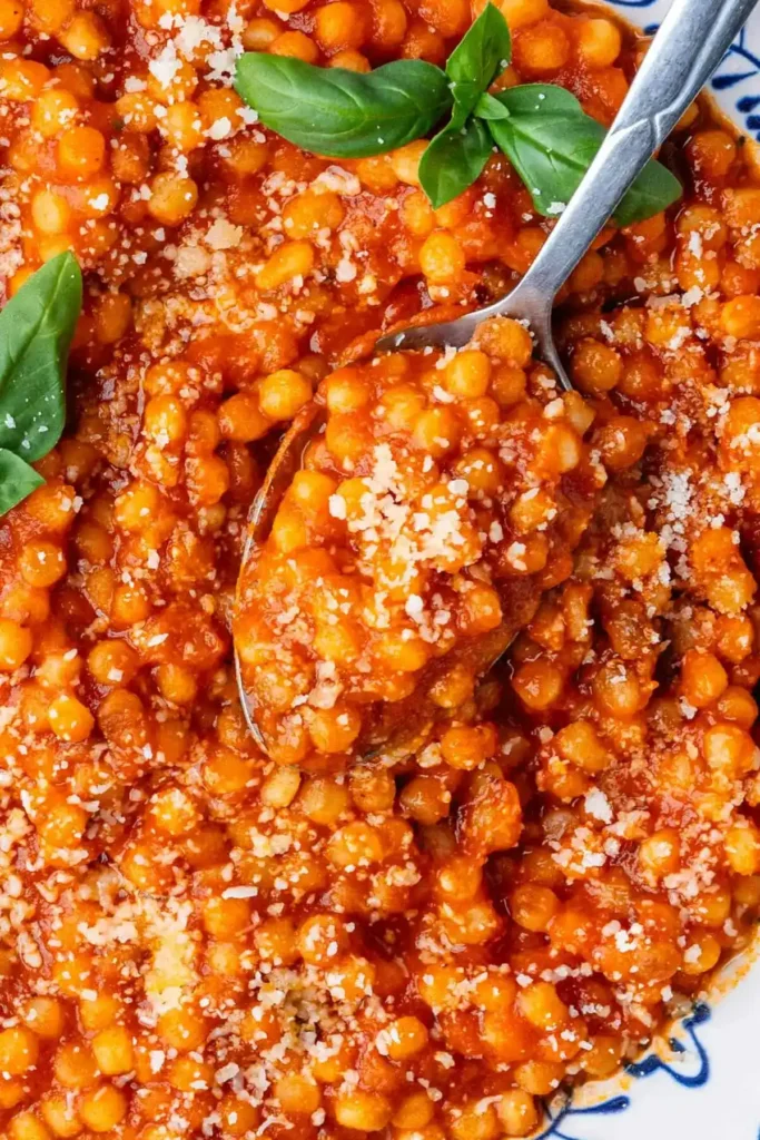 Nahaufnahme von Fregola Sarda in Tomatensoße mit geriebenem Pecorino und frischem Basilikum