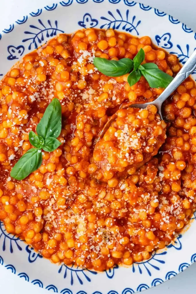 Cremige Fregola Sarda mit Tomatensoße, Parmesan und Basilikum auf einem Löffel