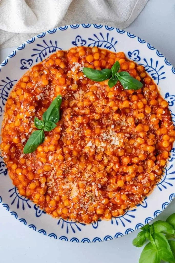 Fregola Sarda mit Tomatensoße, Parmesan und frischem Basilikum auf einem Teller