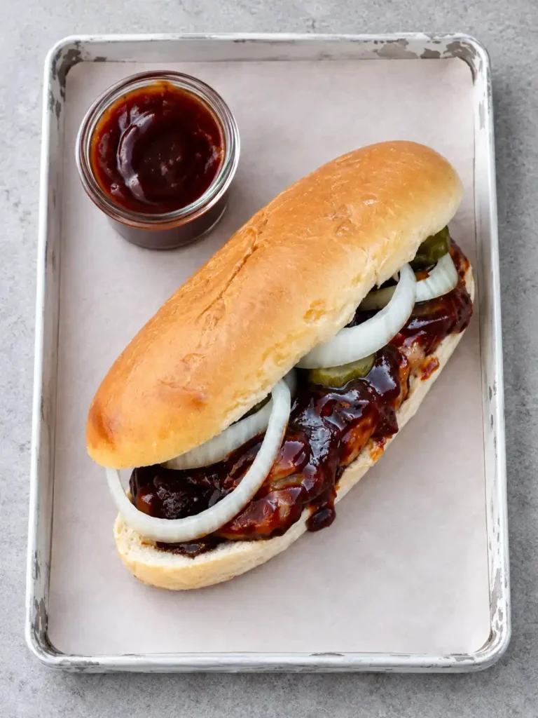 McRib mit BBQ-Soße, Zwiebelringen und Gewürzgurken auf einem weißen Tablett, von oben gesehen.
